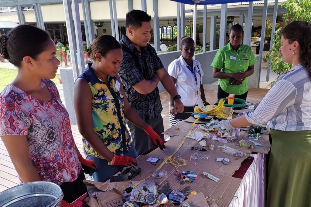 a woman talking to a group of people in front of a table of litter