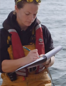 A woman writing on a clipboard whilst wearing a life jacket