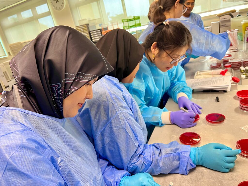 three women in blue lab coats working with petri dishes in a lab