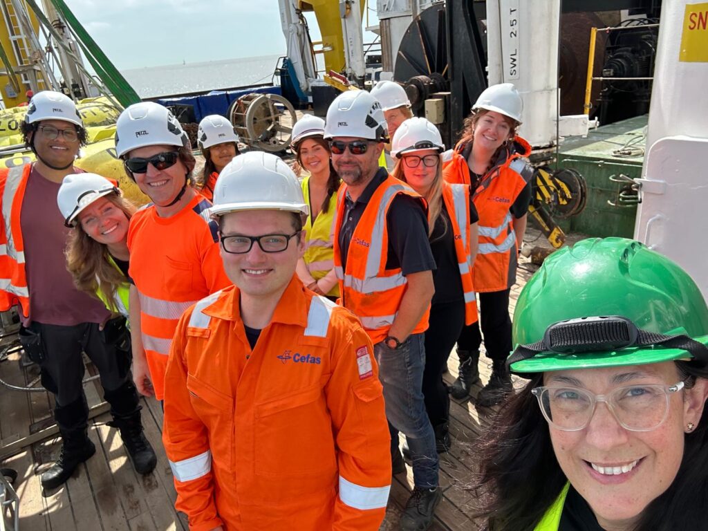 a group of people in orange boiler suits wearing hard hats all smiling on a ship